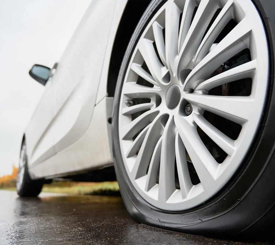 Nahaufnahme eines auf einer nassen Straße geparkten Autos mit einem platten Vorderreifen.