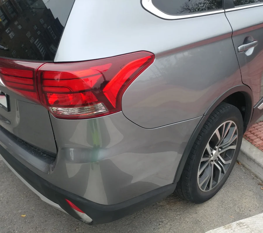 Nahaufnahme der hinteren linken Seite eines grauen Geländewagens, der neben einem Gehweg geparkt ist, wobei das Rücklicht, das Rad und die hintere Tür zu sehen sind.