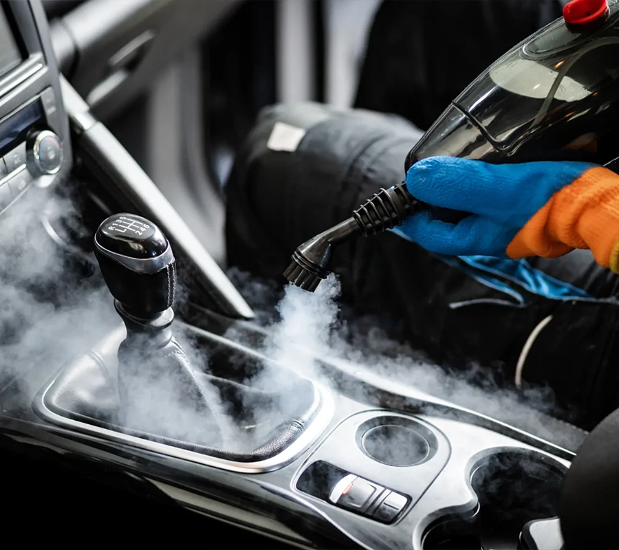 Eine Person, die Handschuhe trägt, desinfiziert mit einem Dampfreiniger den Schalthebel und die Innenkonsole eines Autos.