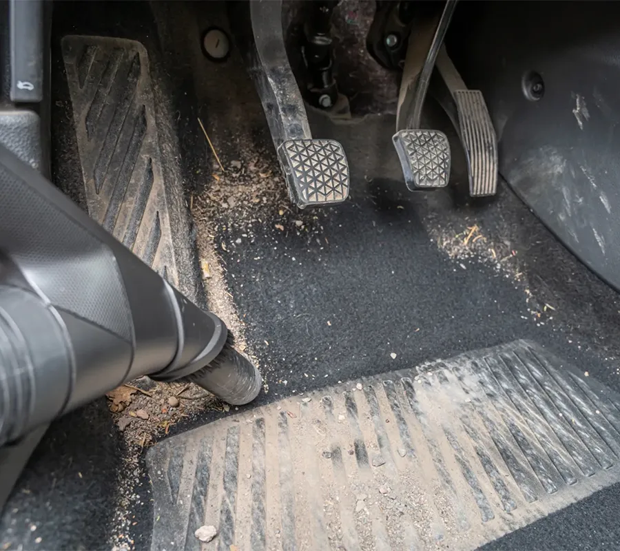 Ein Mann saugt den Vordersitz eines Autos und konzentriert sich dabei auf den Bereich zwischen den Sitzen mit einem Handstaubsauger für gründliche innenraumpflege und auto reinigung.